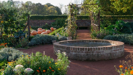 The kitchen garden at Packwood, Warwickshire in autumn. Paths lead off a central circular pond with beds growing flowers and vegetables between the paths. A group of large pumpkins can be seen.